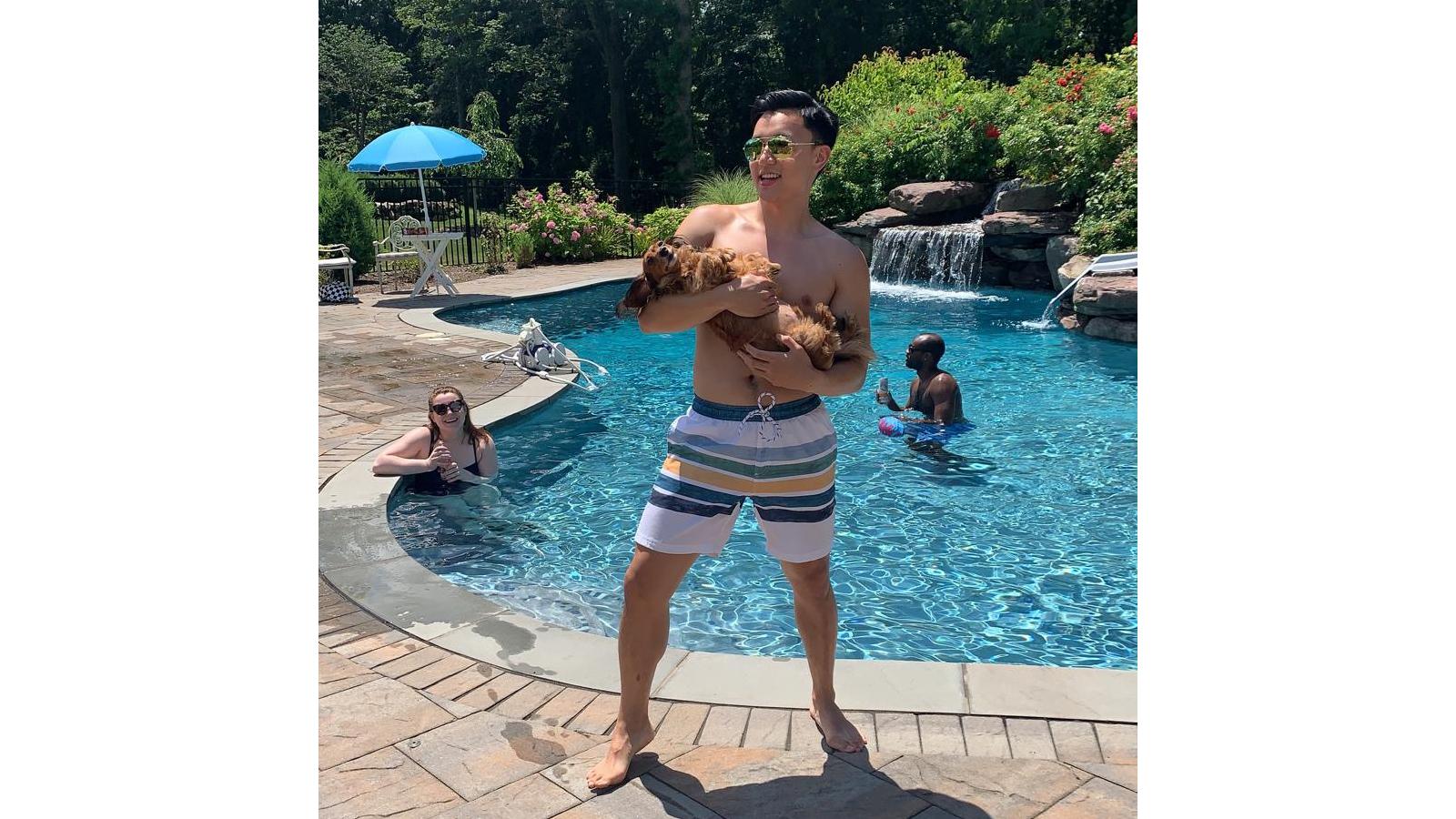 Man holding puppy in front of a swimming pool