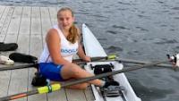 Teen athlete Leila sits on the dock next to her single scull (narrow shell for a single rower).