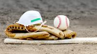 Baseball glove, ball, and medical mask on pitcher's mound.